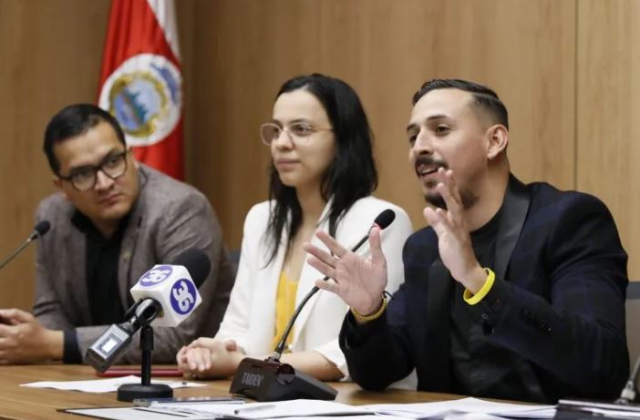 tres personas hablando en escritorios con microfono