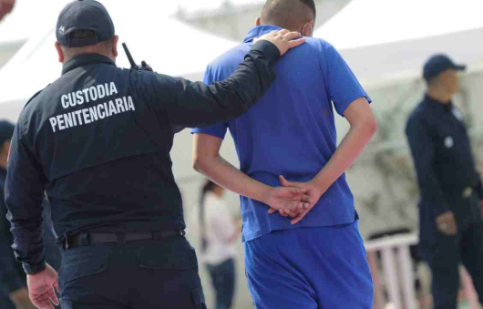 Persona encarcelda sigiendo conducida por un policia de reforma.