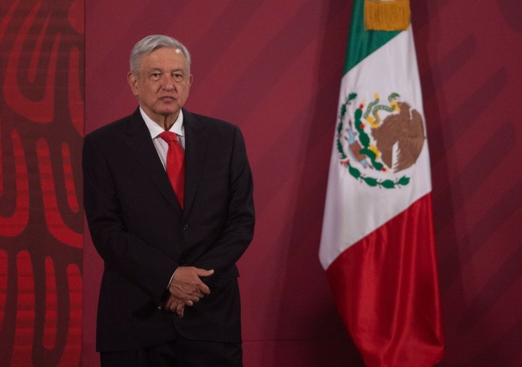 Presidente AMLO de pie frente a banderas