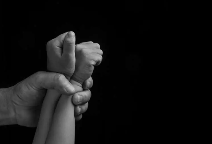 Mano adulta sujetando manos de ni&ntilde;o.